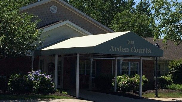 The entrance of a building with an awning, surrounded by greenery on a sunny day.