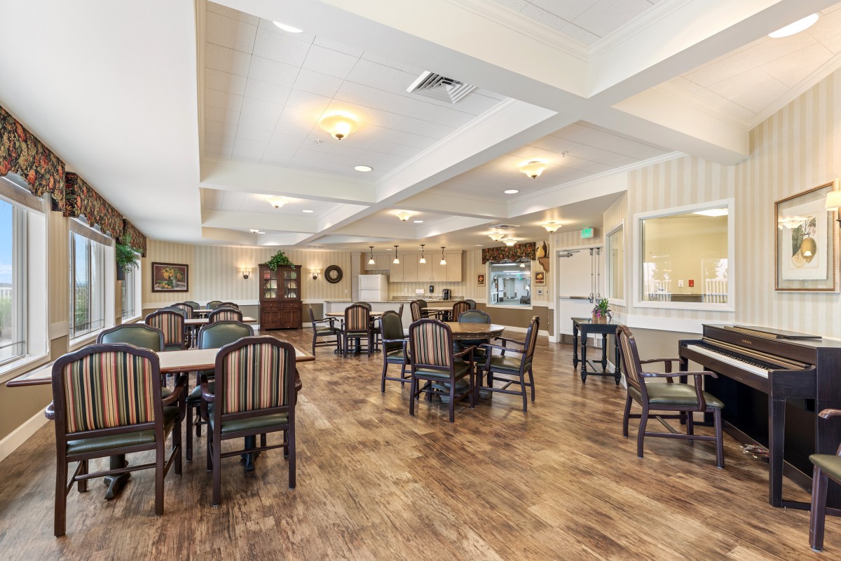 A spacious dining room with multiple tables and chairs, featuring wood flooring and ceiling lights.