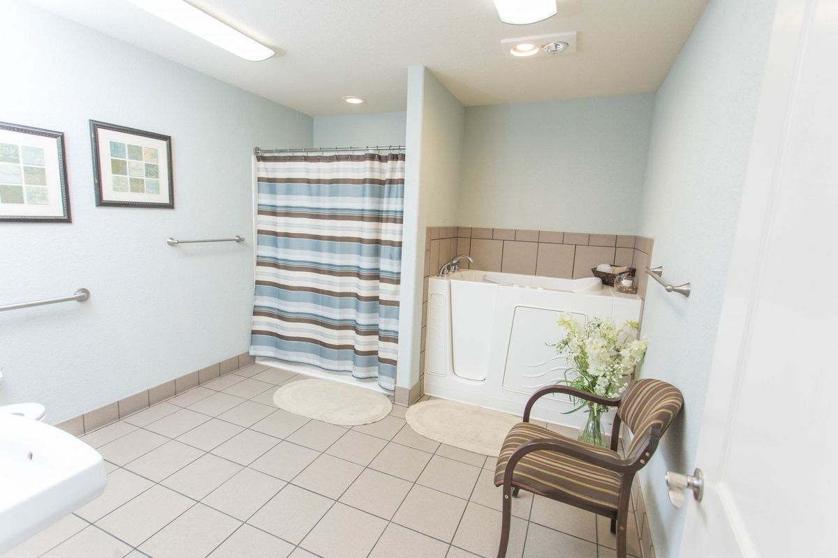 A spacious bathroom with a striped shower curtain, tiled floor, and a small chair beside the sink.