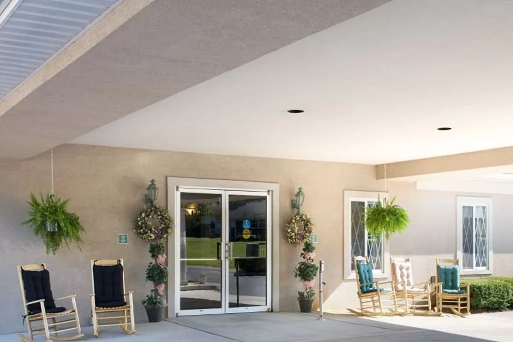 A sunny porch with seating arrangements and decorative plants near an entrance with glass doors.