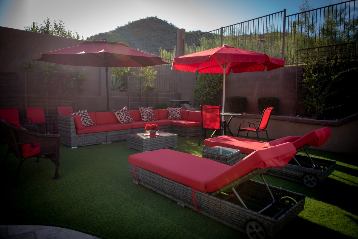 A cozy backyard patio setup featuring red lounge chairs and umbrellas with a view of the mountains in the background.