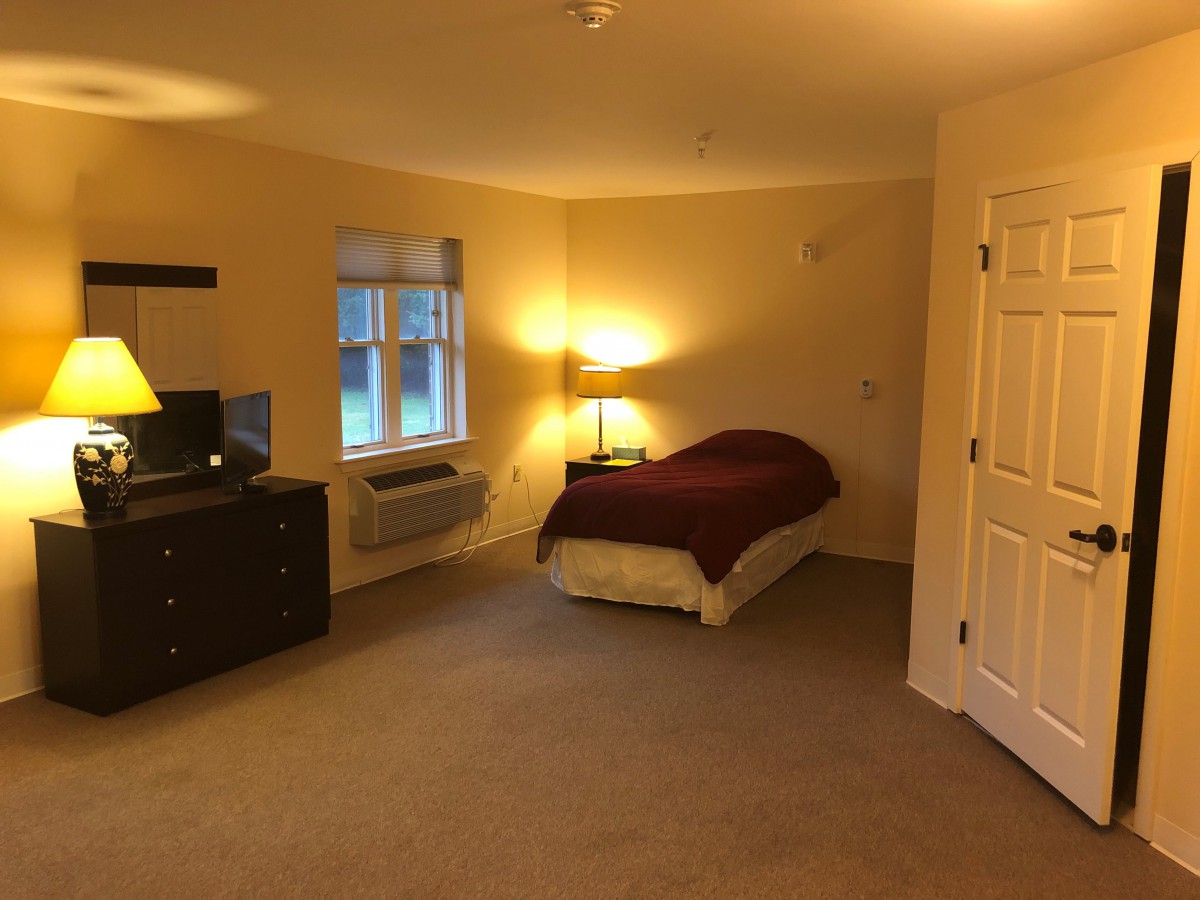 A cozy bedroom with a single bed, lamp, dresser, and window.