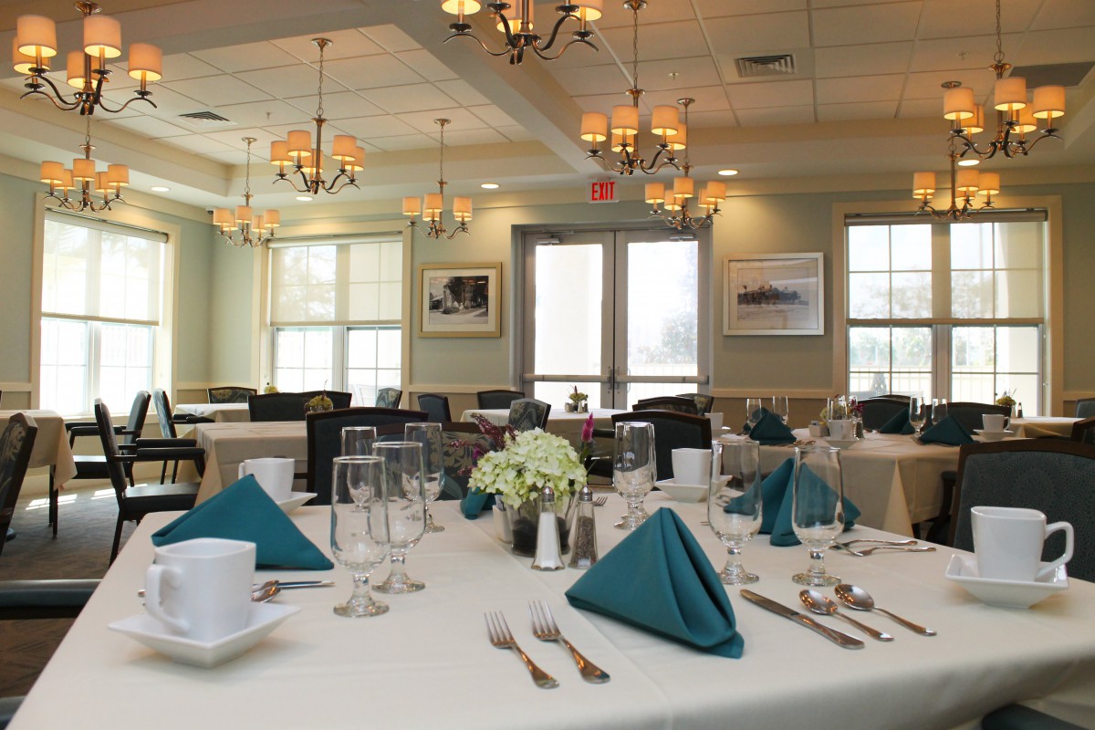 Elegantly set dining room with neatly arranged tables and teal napkins.