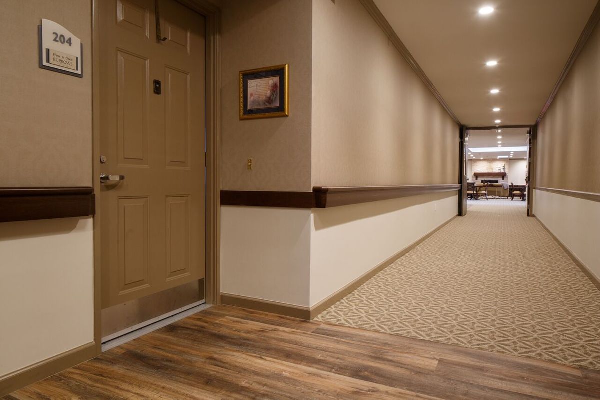 A well-lit hotel hallway with a wooden floor and carpet, featuring a closed door on the left.