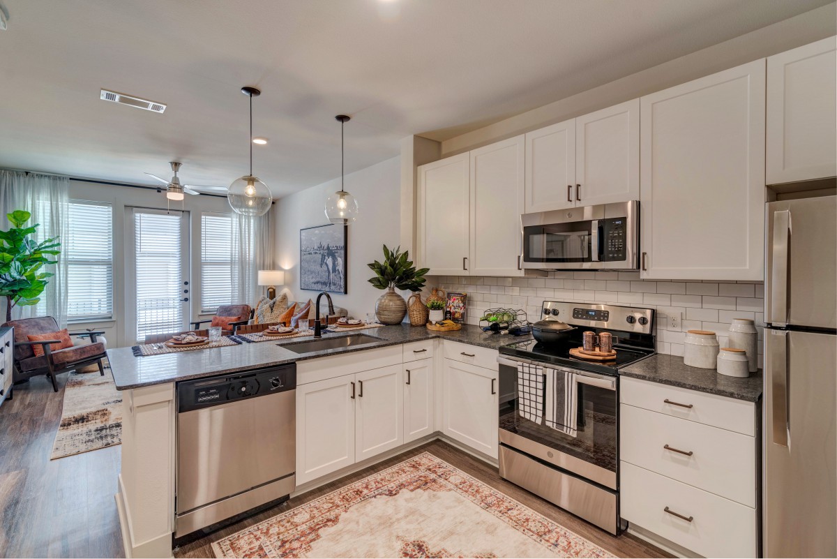 A modern kitchen with white cabinets and stainless steel appliances, featuring an island countertop and stylish pendant lighting.