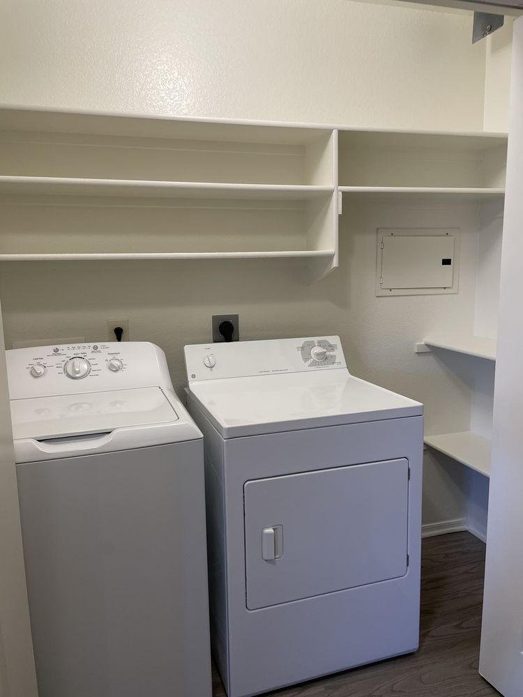 A clean laundry room with a washer, dryer, and shelving.
