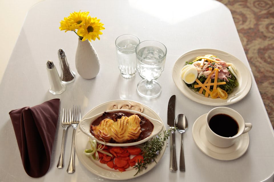 A table setting featuring a hearty meal with pasta, salad, and coffee alongside fresh yellow flowers.
