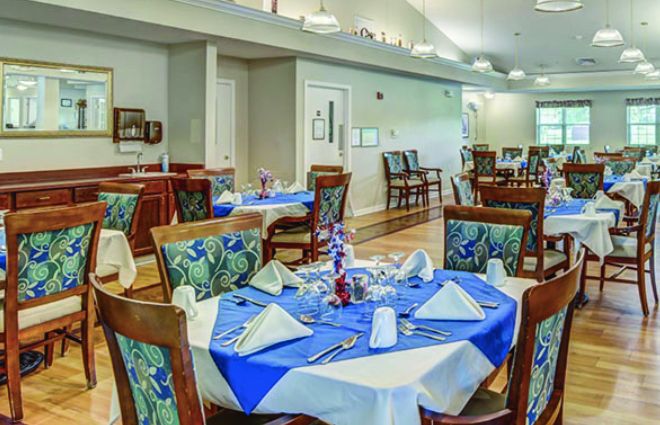 A neatly arranged dining room with tables set, featuring blue and white tablecloths and decorative napkins.