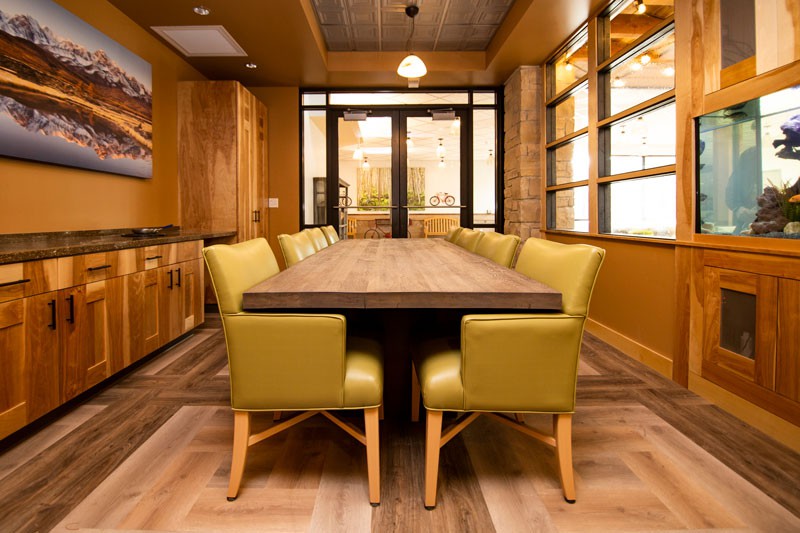A modern dining room with a wooden table and green chairs, accented by ample natural light from large windows.