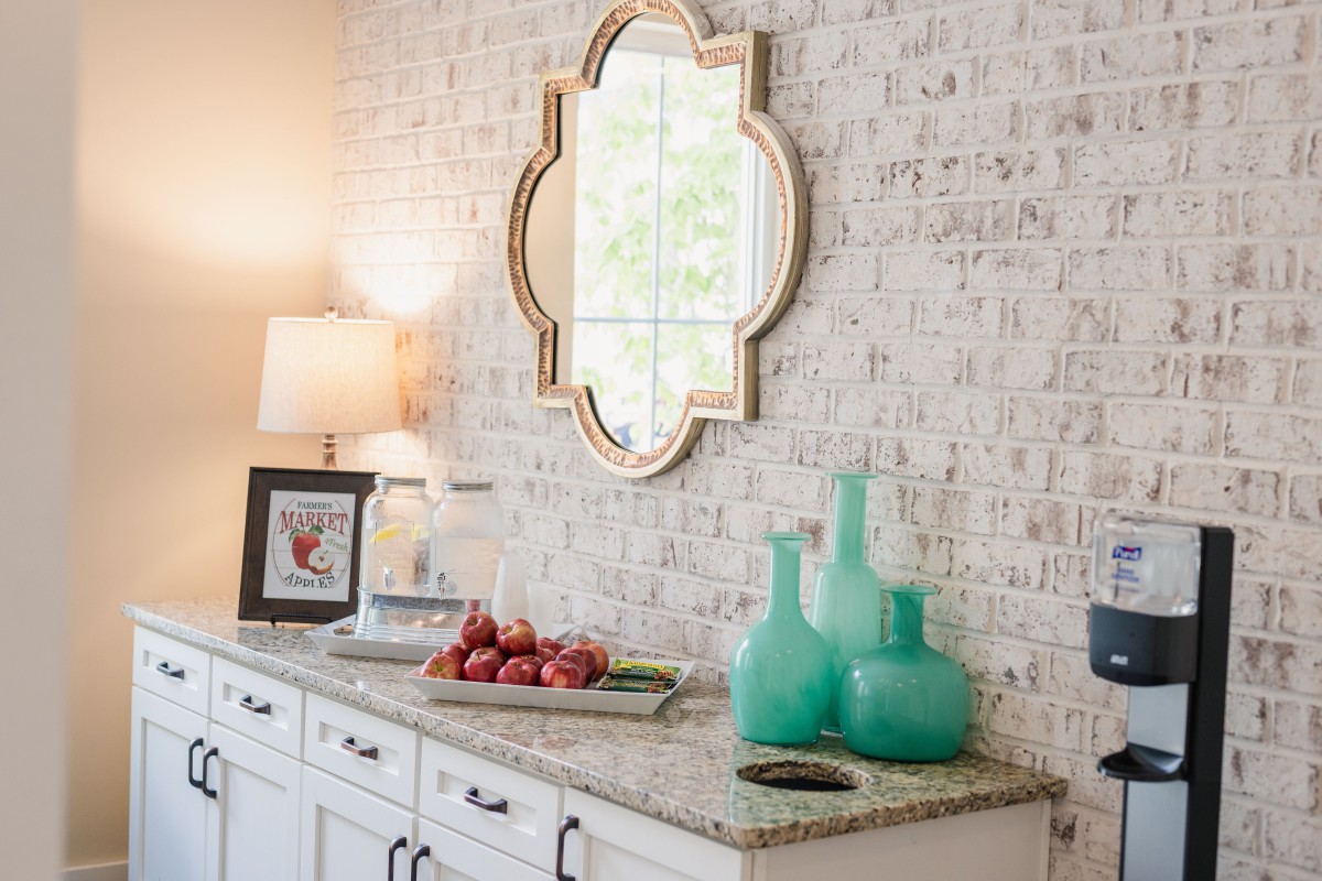 A stylish interior features a sideboard with decorative vases, a lamp, and a unique mirror on a brick wall.
