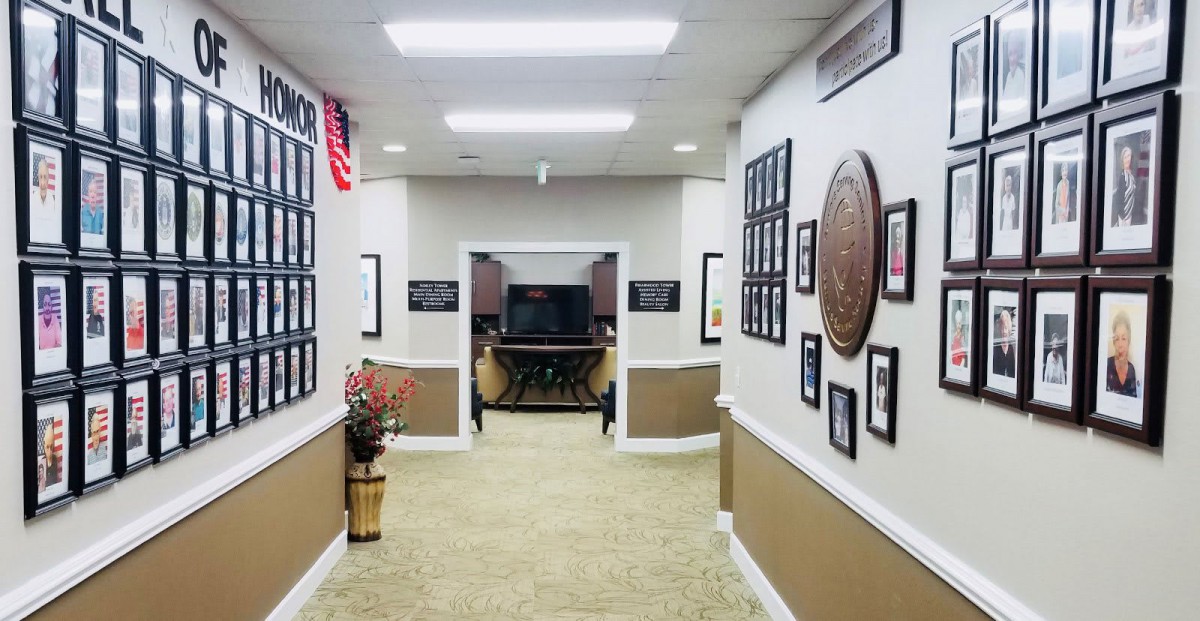 A hallway in an office setting with framed pictures and a flag adorning the walls.