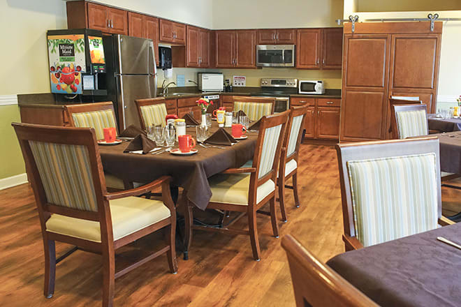 A cozy kitchen and dining area with a wooden table set for a meal, surrounded by chairs on a polished wooden floor.
