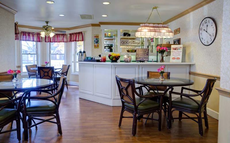 A cozy cafe interior with tables and chairs, featuring a wooden floor and a decorative counter.