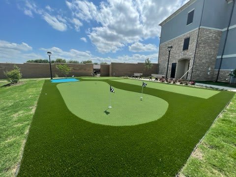 A backyard putting green with artificial turf under a blue sky.