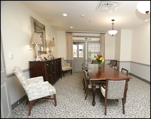 A well-furnished dining room with a long table and upholstered chairs, featuring elegant decor and soft lighting.