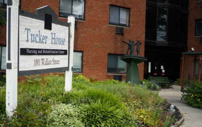 Entrance of a brick building with a sign and a statue surrounded by greenery.