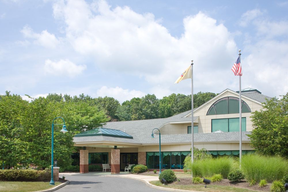 A view of a building entrance with flags flying and a driveway leading up to it, surrounded by trees under a partly cloudy sky.