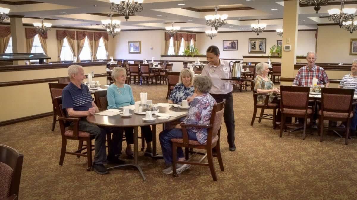 A group of seniors being served by a waiter in a spacious dining area.