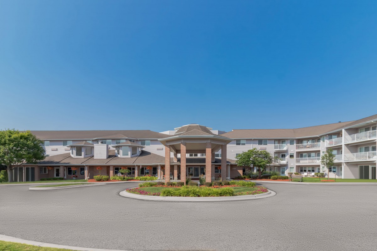 Exterior view of a multi-story residential building with a landscaped entrance and driveway.