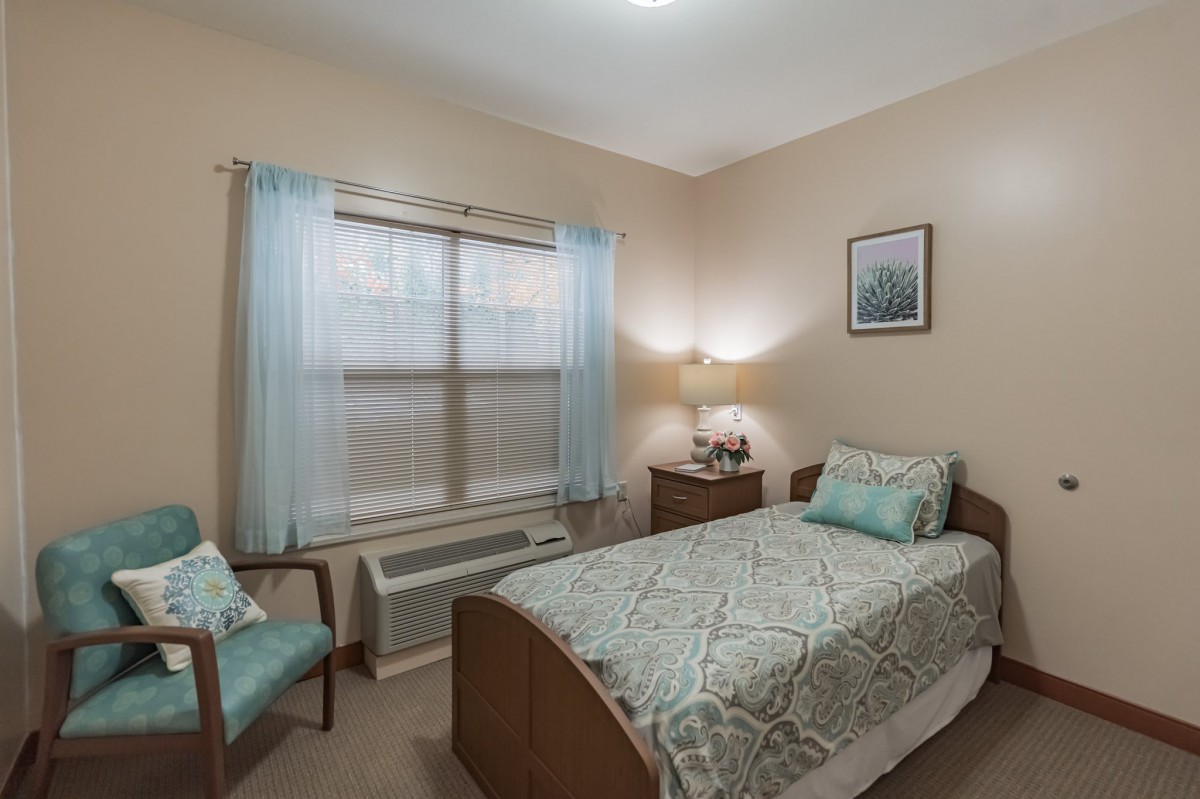 A cozy bedroom with a single bed, window with curtains, and a bedside lamp.
