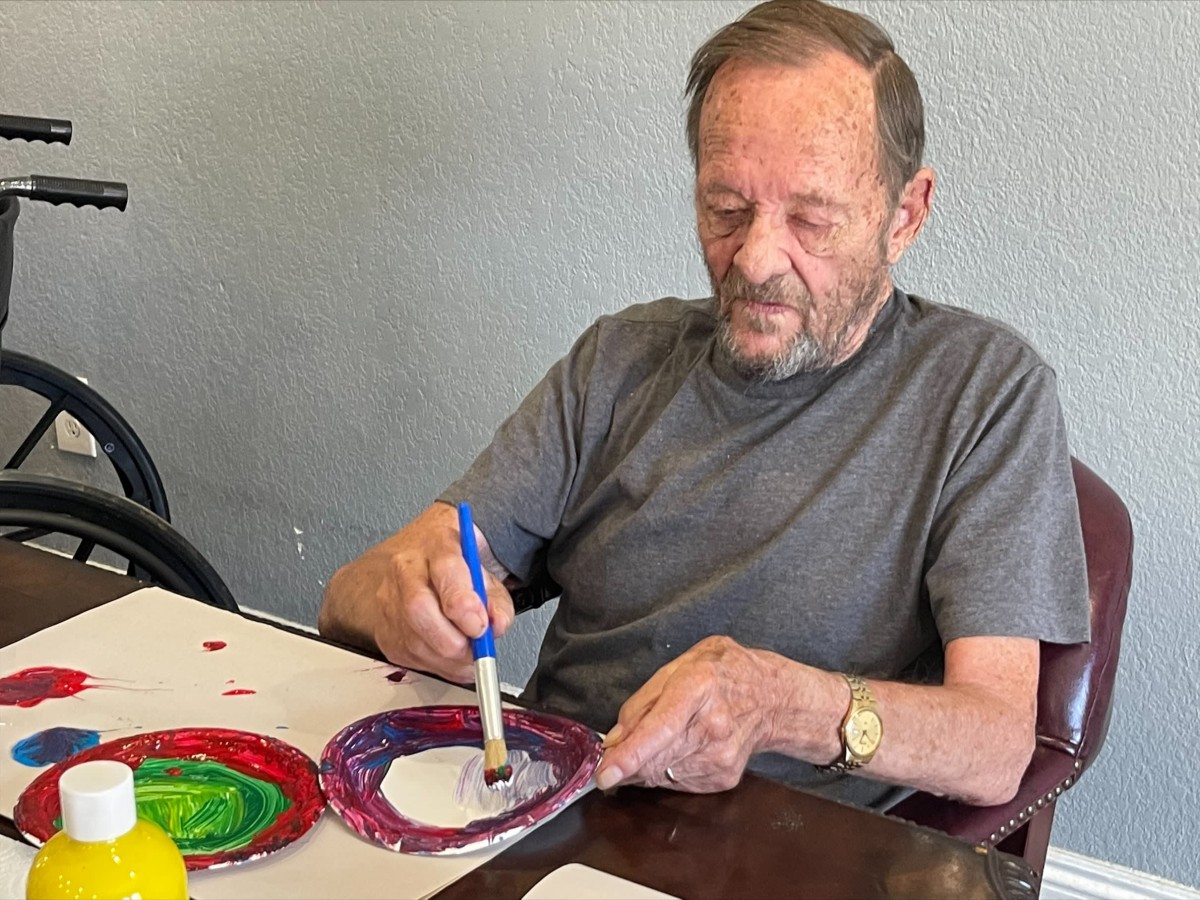 A man engaged in painting with brushes at a table, creating colorful artwork.