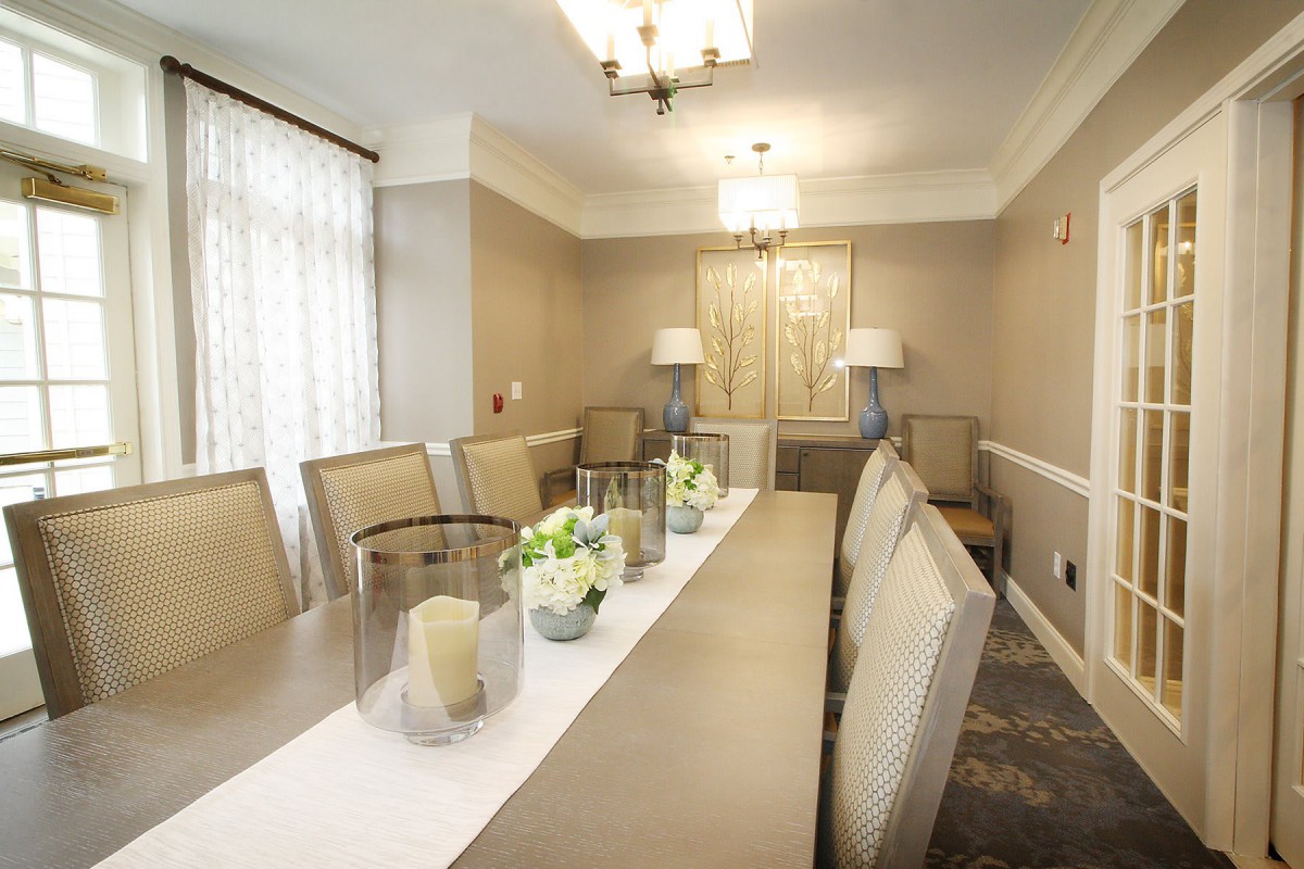 An elegant dining room with a long table, cushioned chairs, and modern lighting fixtures.