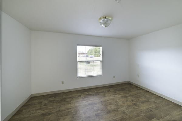 A vacant room with white walls, a single window, and wooden flooring.