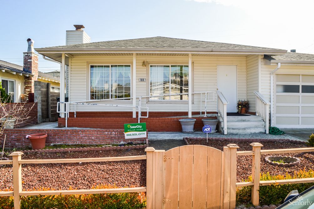 A single-story house with a front porch and small garden, enclosed by a wooden fence.