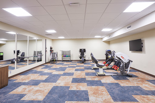 A spacious and well-equipped gym area featuring various exercise machines and a mirrored wall.