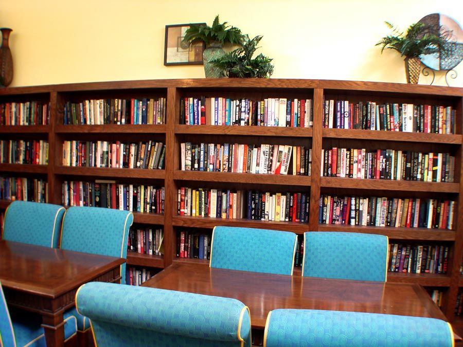 A cozy library room with bookshelves filled with books and blue chairs around a wooden table.