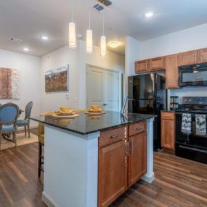 A modern kitchen interior in an apartment featuring wooden cabinets, a black appliance set, and an island counter.