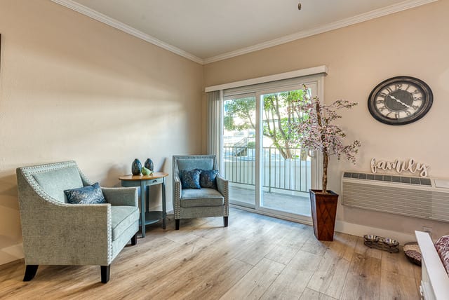 A cozy living room with comfortable seating and natural light streaming through a sliding glass door.
