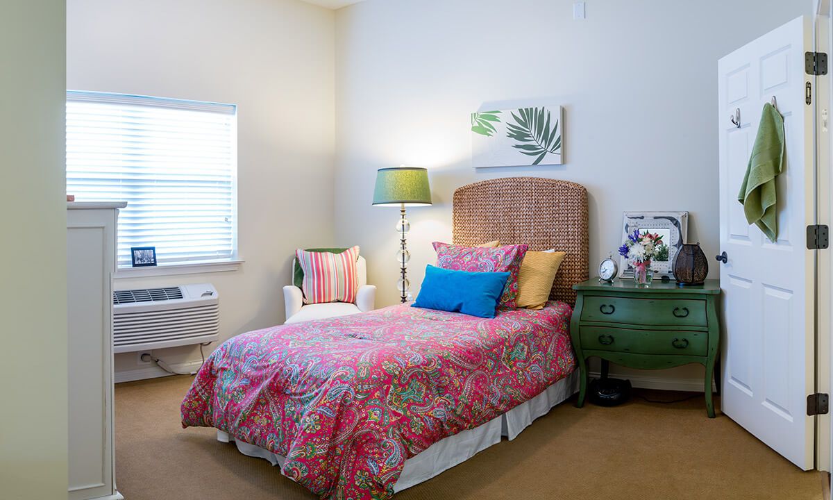 A cozy bedroom with a colorful bedspread, white chair, and green bedside table.
