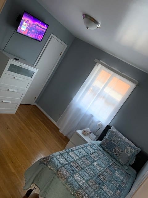 A cozy bedroom with a neatly made bed, a dresser, and a television mounted on the wall.