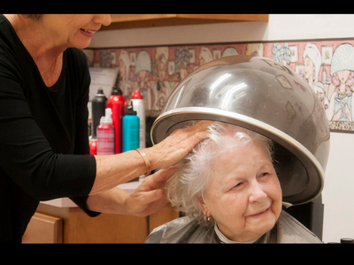 An elderly woman enjoying a hair treatment at a salon, under a heated dryer.