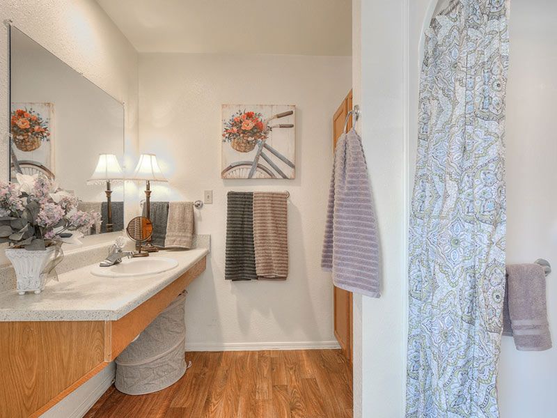A well-decorated bathroom with a wooden floor, featuring a sink area, mirror, and neatly arranged towels.