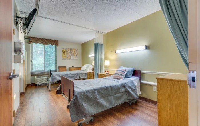 A hospital room with two patient beds, featuring simple furnishings and bright lighting.
