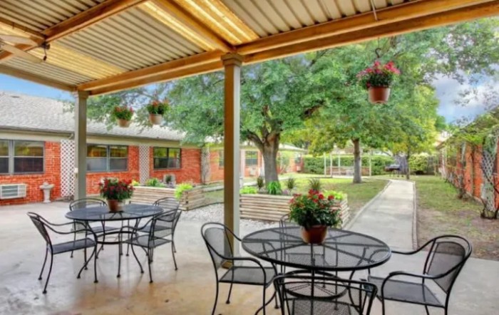 A cozy outdoor patio area with metal tables and chairs, surrounded by greenery.