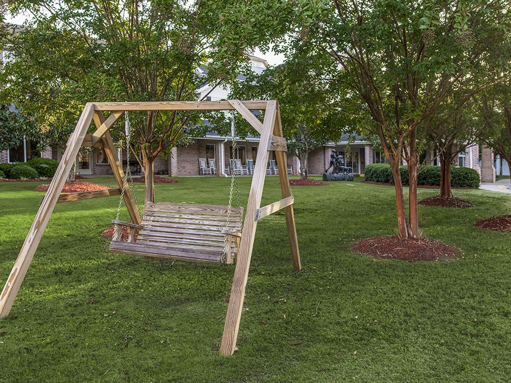 A wooden swing bench in a lush garden setting surrounded by trees and green grass.
