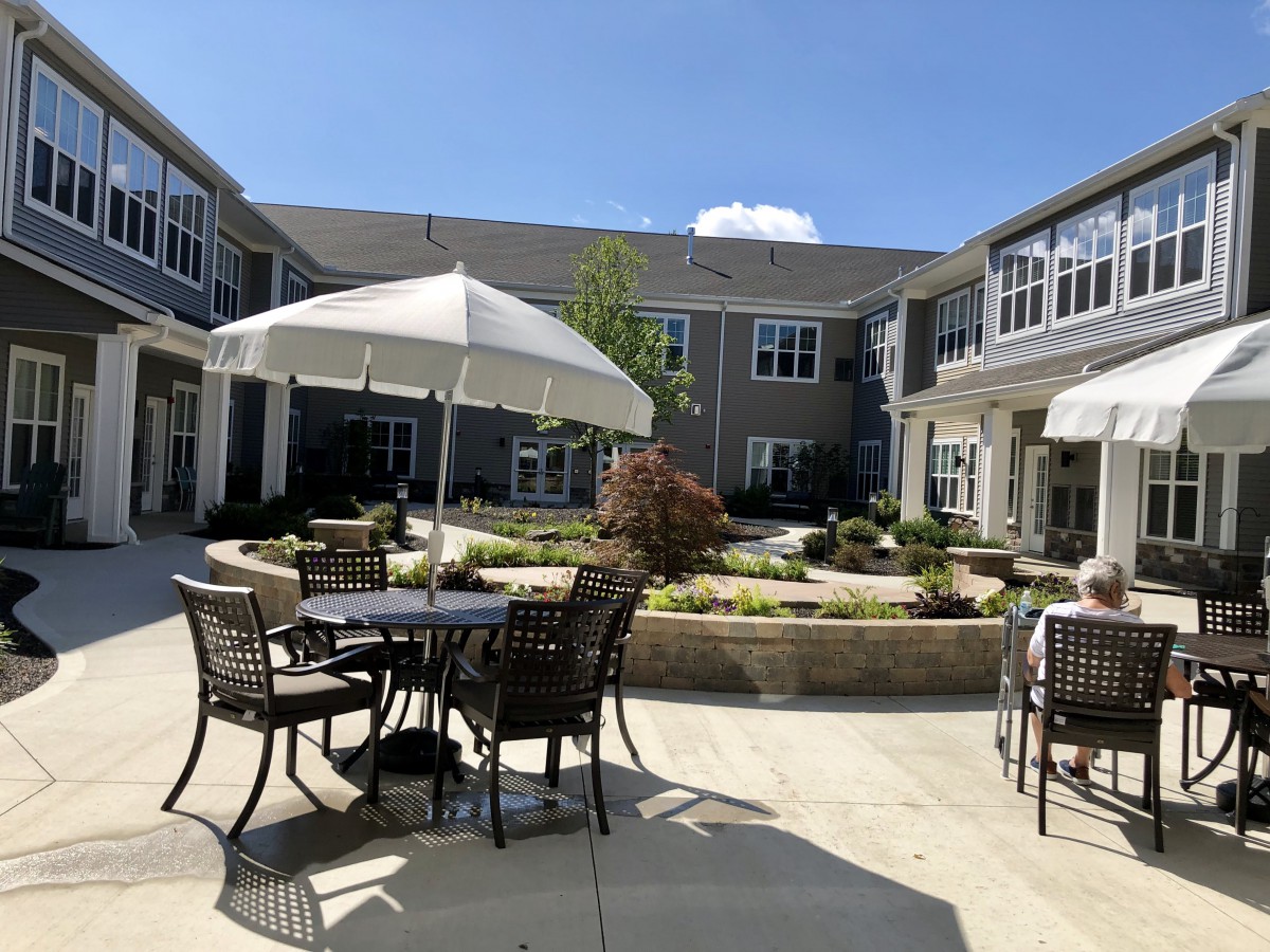 A sunny courtyard with outdoor seating, featuring tables and umbrellas amidst pleasant landscaping.
