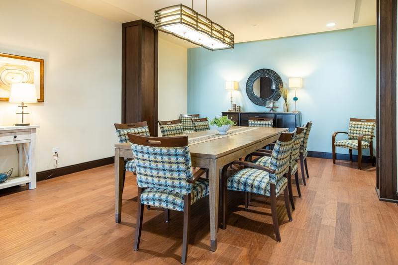 A modern dining room featuring a large wooden table with plaid upholstered chairs, complemented by a stylish light fixture and decorative elements like a mirror and buffet table.