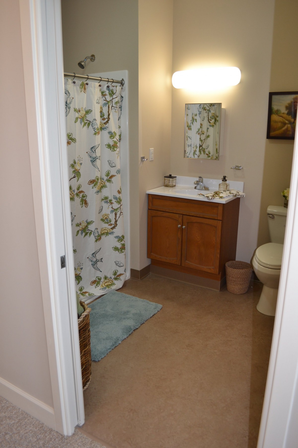 A tidy bathroom with a floral shower curtain and wooden cabinet.