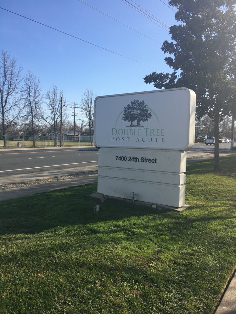 A street sign with a tree logo in a grassy area alongside a road.