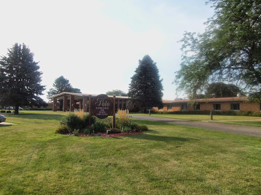 A picturesque view of a building surrounded by lush green grass and trees, featuring a decorative sign in the foreground.