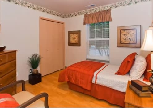A cozy bedroom with a single bed featuring orange bedding, a window with curtains, and decorative artwork on the walls.