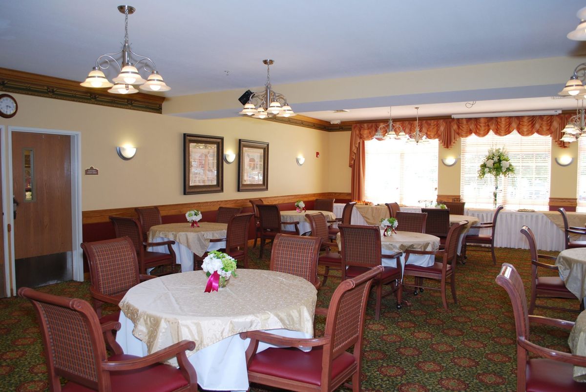 A well-decorated dining room with multiple tables and chairs arranged neatly, featuring chandeliers and floral centerpieces.