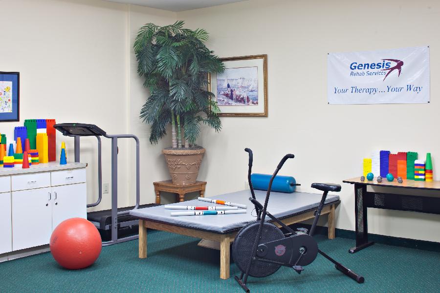 A physical therapy room equipped with a treadmill, stationary bike, therapy table, and an exercise ball.