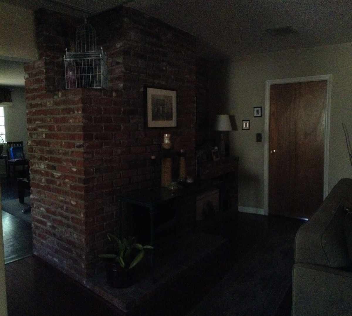 A dimly lit living room featuring a brick wall with a fireplace, a lamp, and a door.