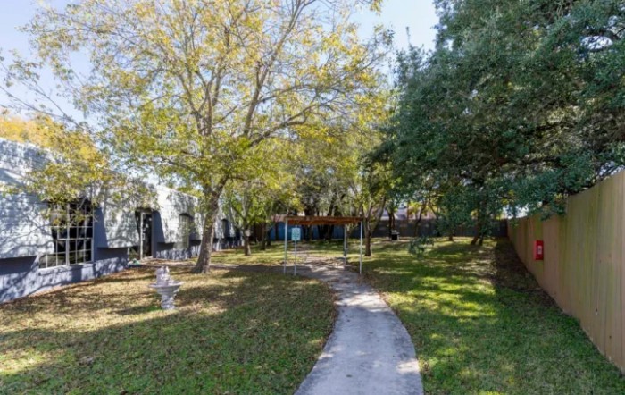 A scenic park pathway shaded by trees and surrounded by green grass.