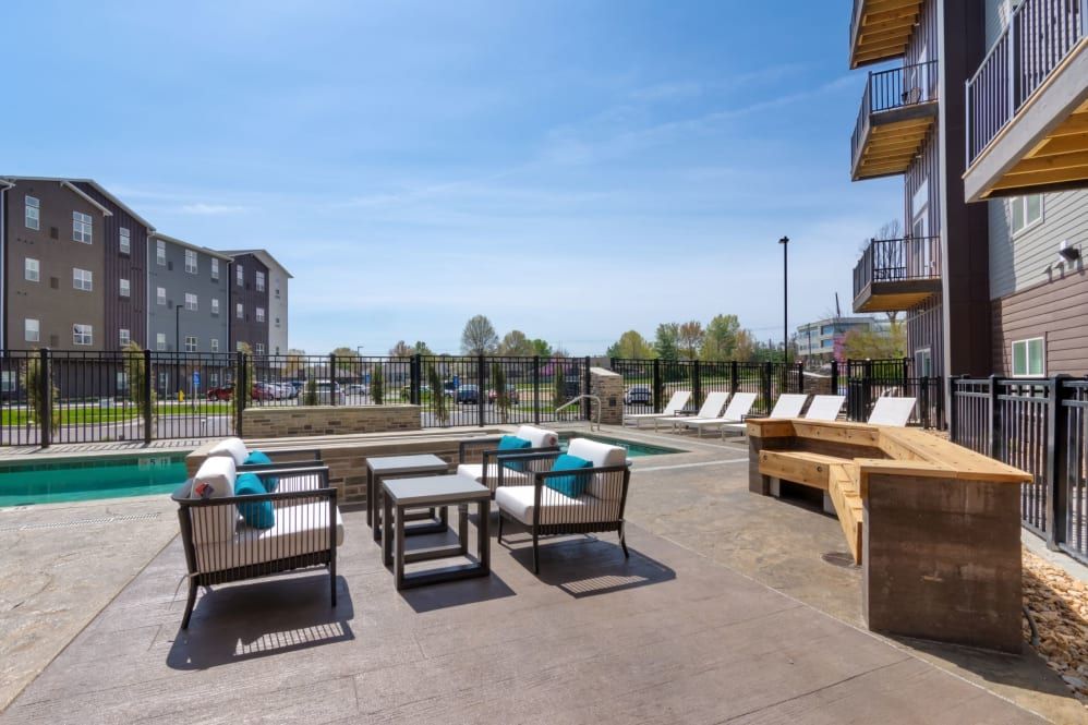 A modern outdoor patio with comfortable seating near a pool at an apartment complex.